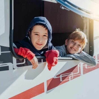 two kids peek out of family travel trailer RV