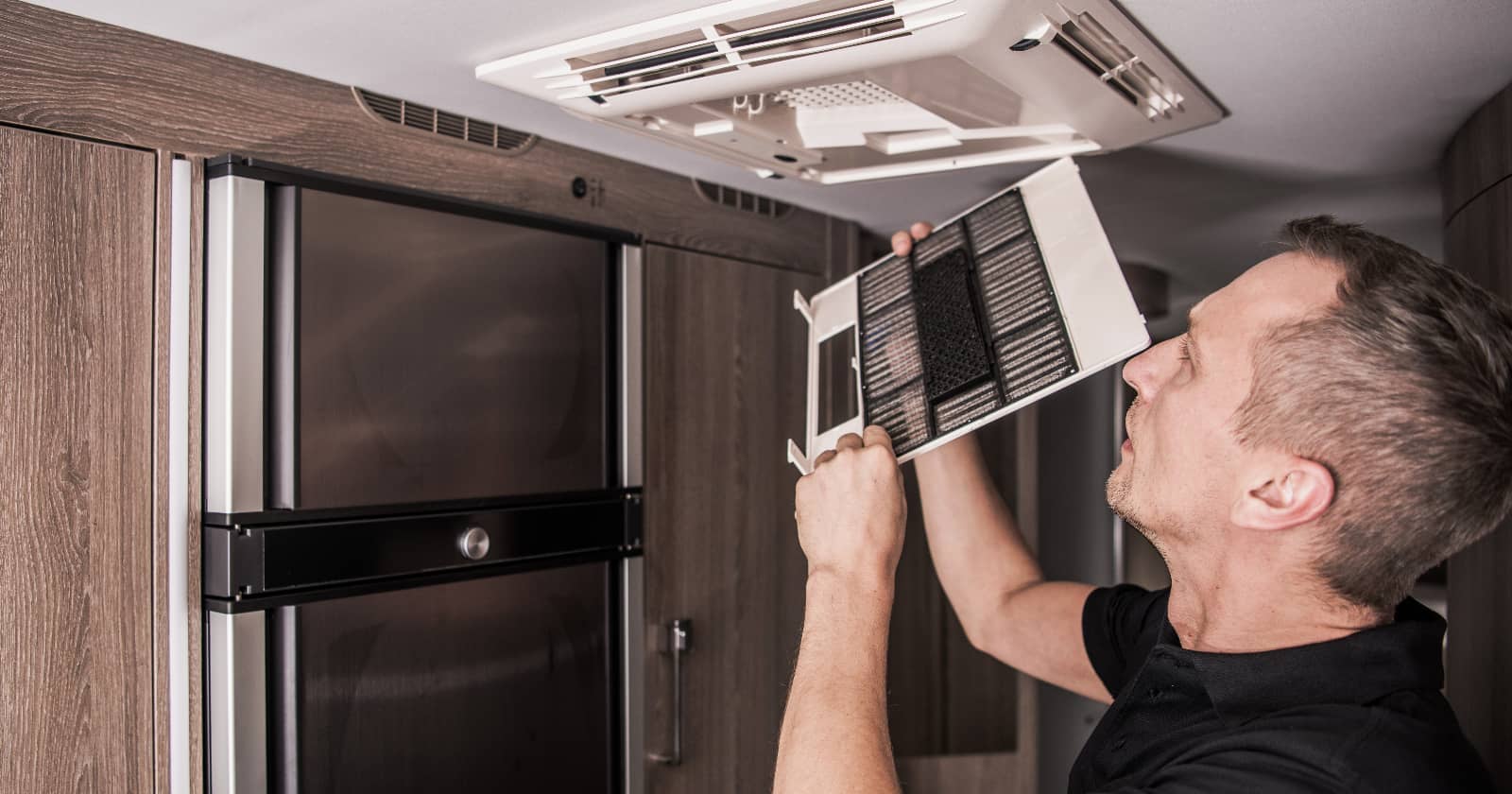 man inspecting RV air conditioner unit from inside an RV