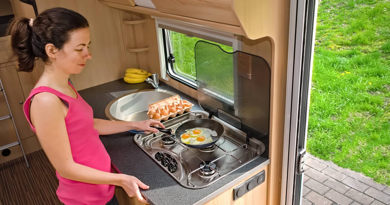 Smiling woman cooking eggs in her RV kitchen