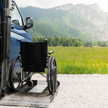 Empty wheelchair on a ramp of a campervan with nature and mountains in the background, RV modifications for disabilities are what help folks get out and travel