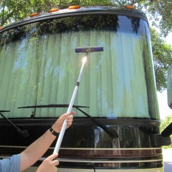 man uses extension to clean a motorhome windshield
